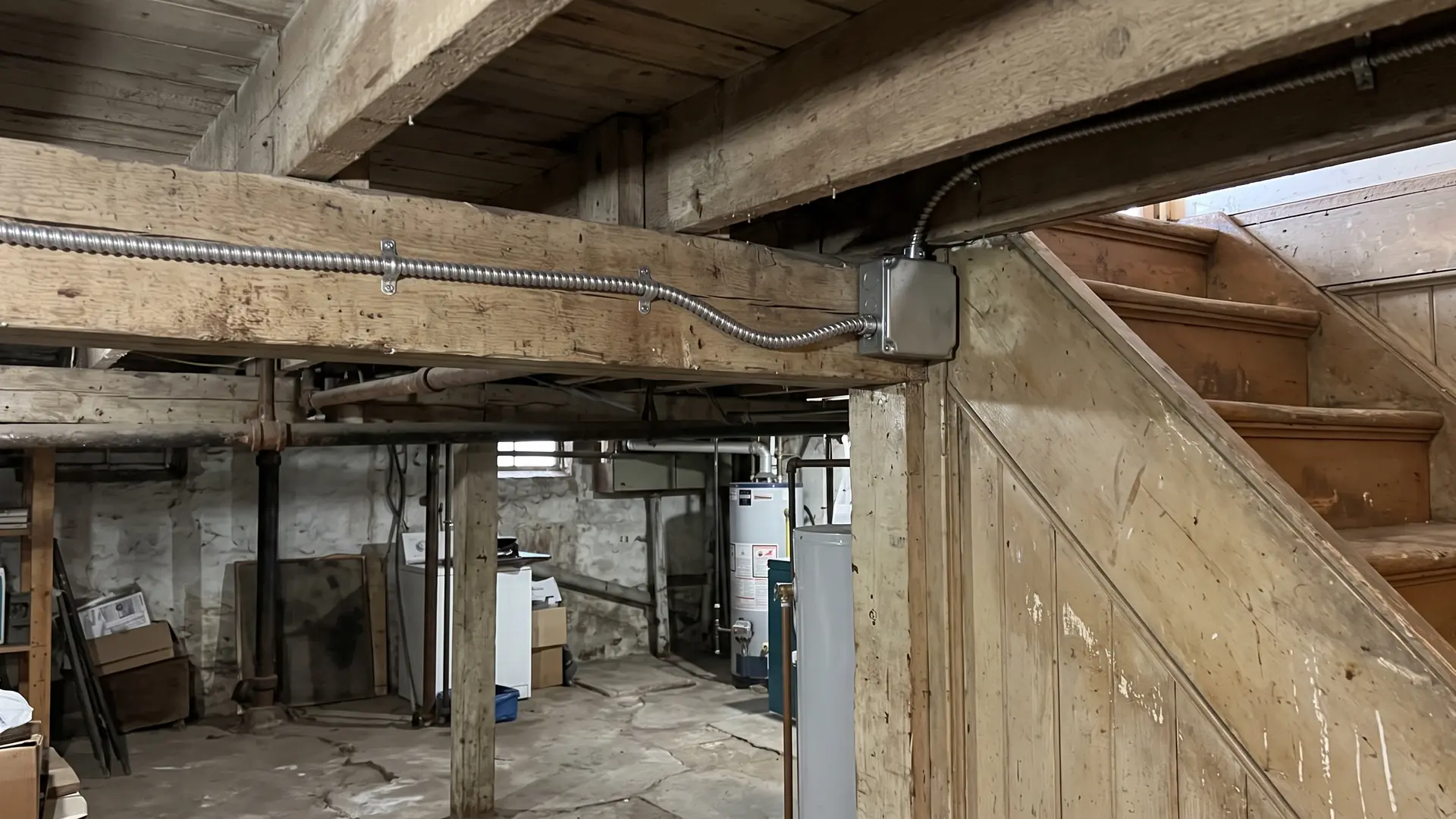 A supported cable along the basement ceiling near an enclosed stair in an older NYC house.