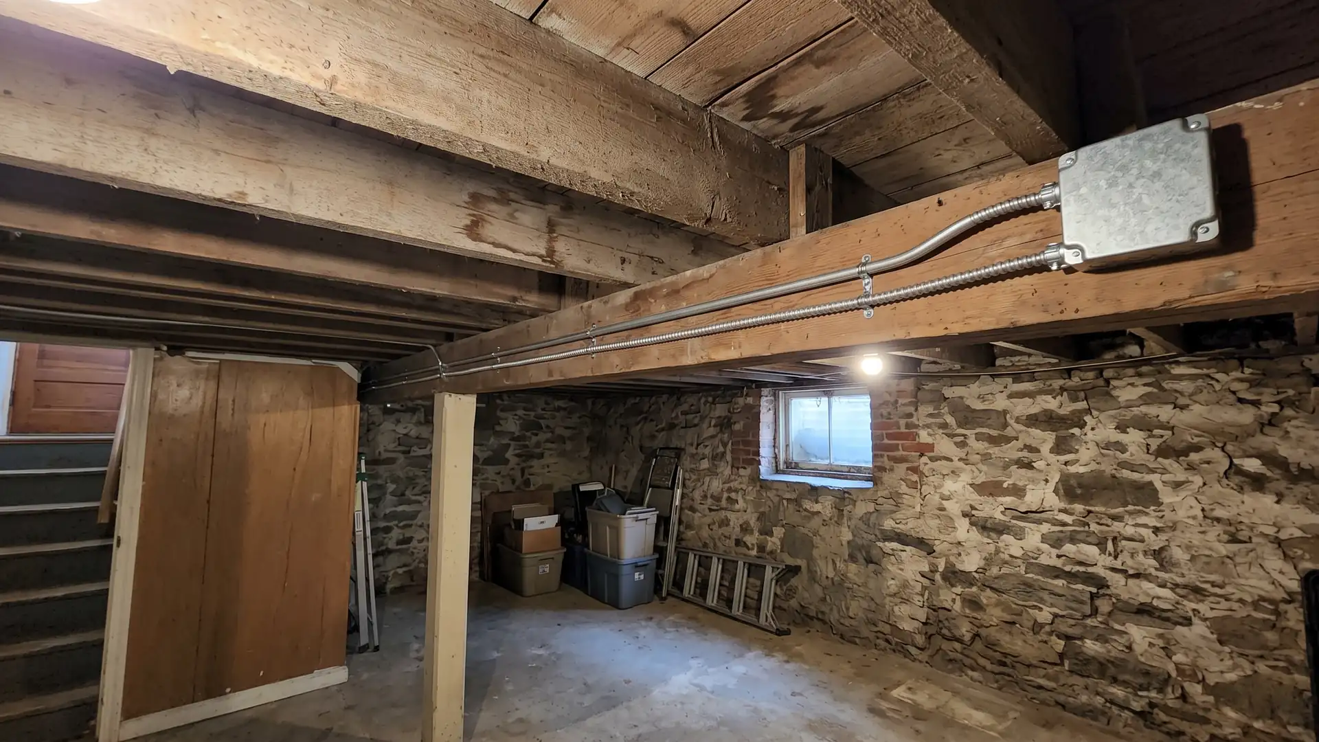 Supported metal-clad cable routes along an older NYC basement ceiling.